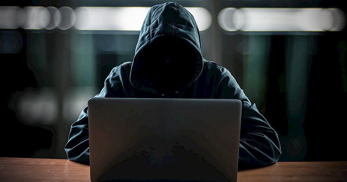 hacker wearing hoodie typing on laptop computer