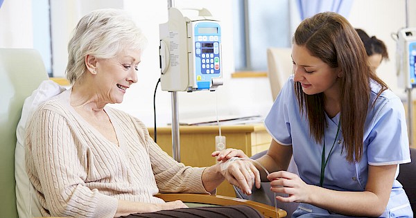 Nurse assisting elderly patient with infusion pump in hospital room