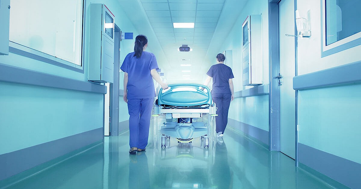 Nurses walking down hospital hallway rolling hospital bed