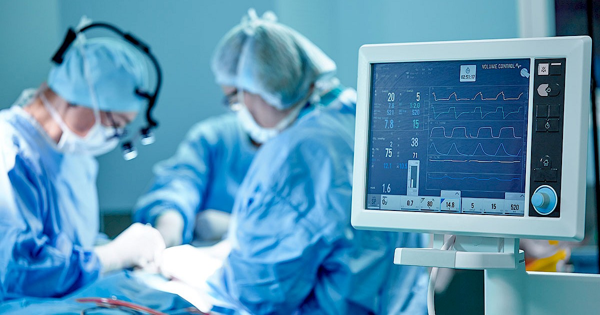 doctors performing surgery with heart monitor screen in foreground