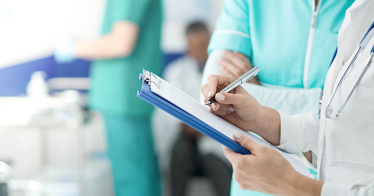 Close up photo of doctor writing on clipboard in hospital room