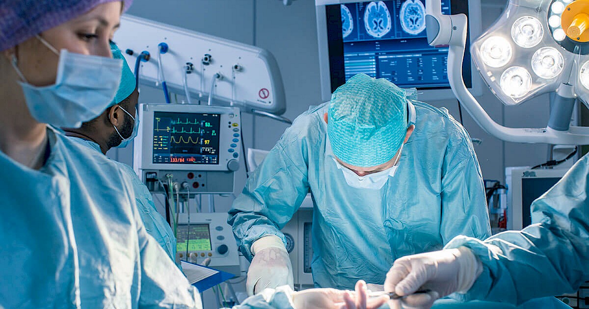 Close up on surgeon performing surgery in operating room surrounded by other doctors all wearing scrubs